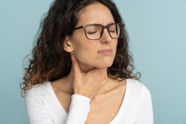 Woman havin<em></em>g sore throat, tonsillitis, feeling sick, suffering from painful swallowing, angina, strong pain in throat, loss of voice, holding hand on her neck, isolated on studio blue background.